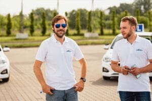 Dwóch instruktorów nauki jazdy stoi na placu manewrowym obok samochodów szkoleniowych i rozmawia.