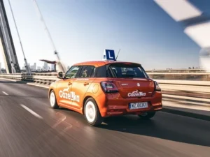 Pomarańczowy samochód szkoły nauki jazdy Gazelka z oznaczeniem L jedzie po moście.